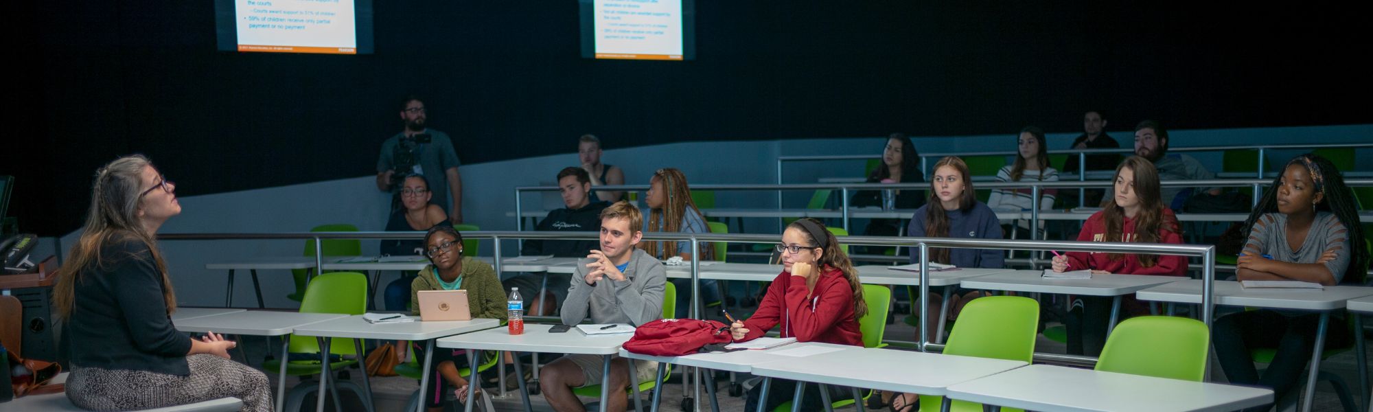 Student sitting in the middle of a lecture, professor is sitting on her desk