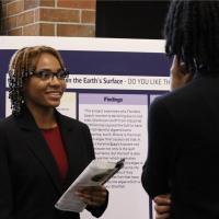 Student presenting research project board at Undergraduate Research Symposium.